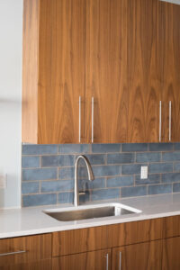 Walnut cabinetry with blue subway tile backsplash and stainless sink.
