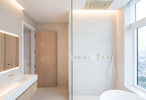 Modern NYC apartment bathroom with glass shower, white oak door, and city view window.