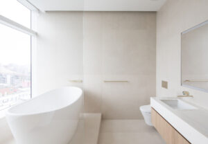 Minimalist bathroom interior with large-format tiles and Manhattan skyline view, featuring a freestanding tub and wooden vanity details in Skyline Tower.