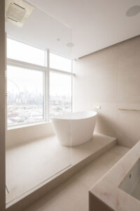 Minimalistic high-rise bathroom with freestanding tub and New York City skyline view through large window.