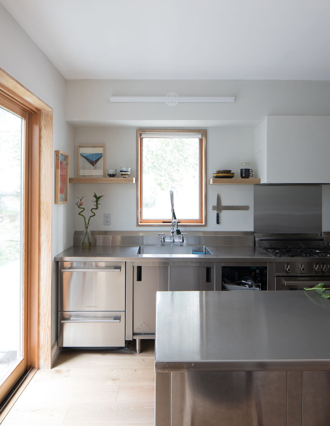 Stainless steel kitchen island and cabinetry with natural wood-framed window in Manhattan townhouse by Rauch Architecture.