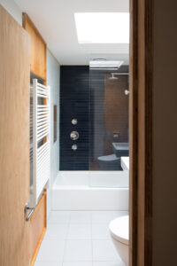 Modern Manhattan townhouse bathroom with dark tiled shower, skylight, and wooden details by Rauch Architecture.