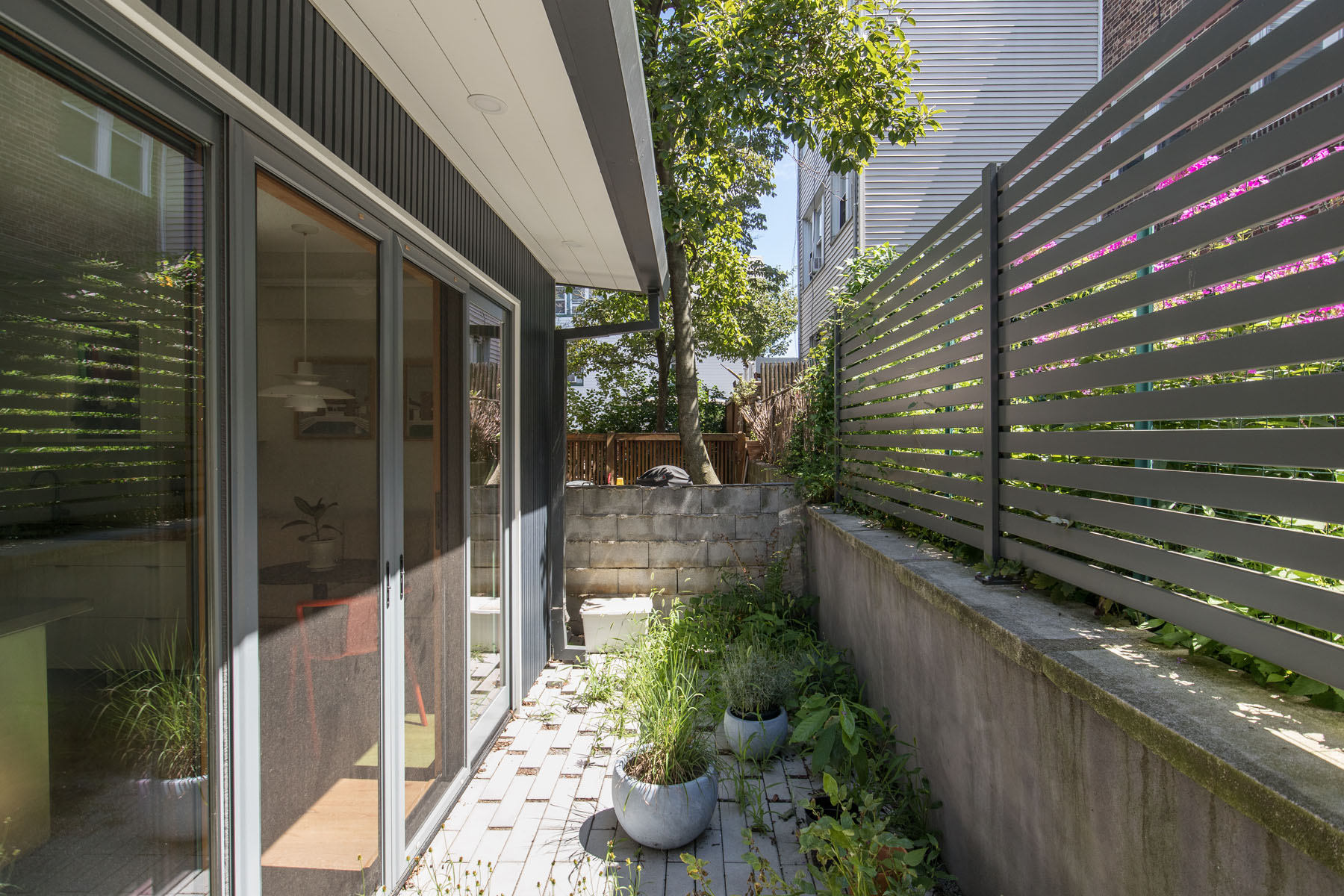 Manhattan townhouse patio with horizontal slat fencing, paving stones, and outdoor planters viewed from sliding glass doors by Rauch Architecture.