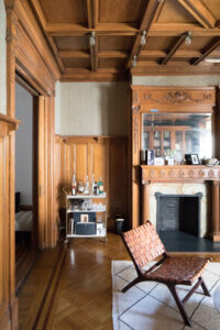 Historic room in Obama Townhouse Park Slope featuring intricate wooden paneling, herringbone flooring, ornate fireplace, and modern bar cart.