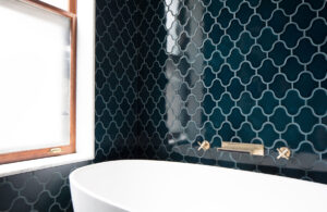 Modern bathroom with teal geometric wall tiles, freestanding white bathtub, and wooden window frame in Obama Townhouse Park Slope.