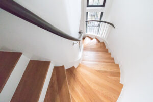 A sweeping view down a curved staircase with oak treads and contrasting dark handrail in a Rauch Architecture-designed Park Slope townhouse.