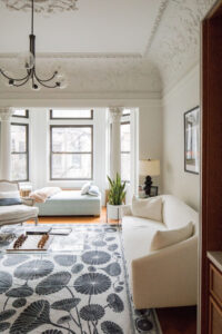 Elegant living space in a Park Slope townhouse with decorative ceiling moldings, bay windows providing natural light, and a botanical-themed area rug, designed by Rauch Architecture.