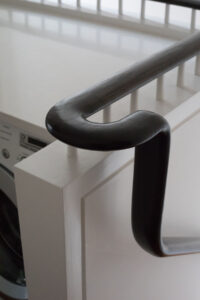Detailed view of a custom-designed dark-stained handrail and baluster atop a white-painted stair newel post in a Rauch Architecture-renovated Park Slope brownstone.