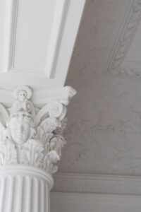 Detail of intricate white Corinthian column capital and ornate ceiling plasterwork in a restored Park Slope townhouse by Rauch Architecture.