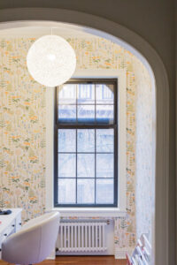 Park Slope townhouse corner with a large arched window, white-framed and set against a wallpapered wall with a botanical pattern, featuring a spherical pendant light, by Rauch Architecture.