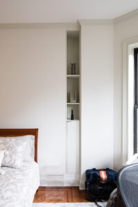 Custom built-in vertical shelving unit in a Park Slope bedroom, with white finish and minimalist decor, designed by Rauch Architecture for efficient space use.