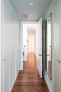 Long, narrow corridor in a Park Slope townhouse designed by Rauch Architecture, featuring hardwood flooring, white paneled doors, and a row of mirrored cabinets reflecting light.