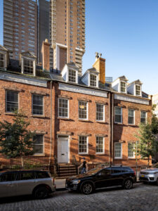 Exterior view of a renovated 1820s Federal Style townhouse in NYC's historic Tribeca townhouse on Harrison Street, showcasing classic brickwork, white trimmed windows, and skylights with pediment detailing.