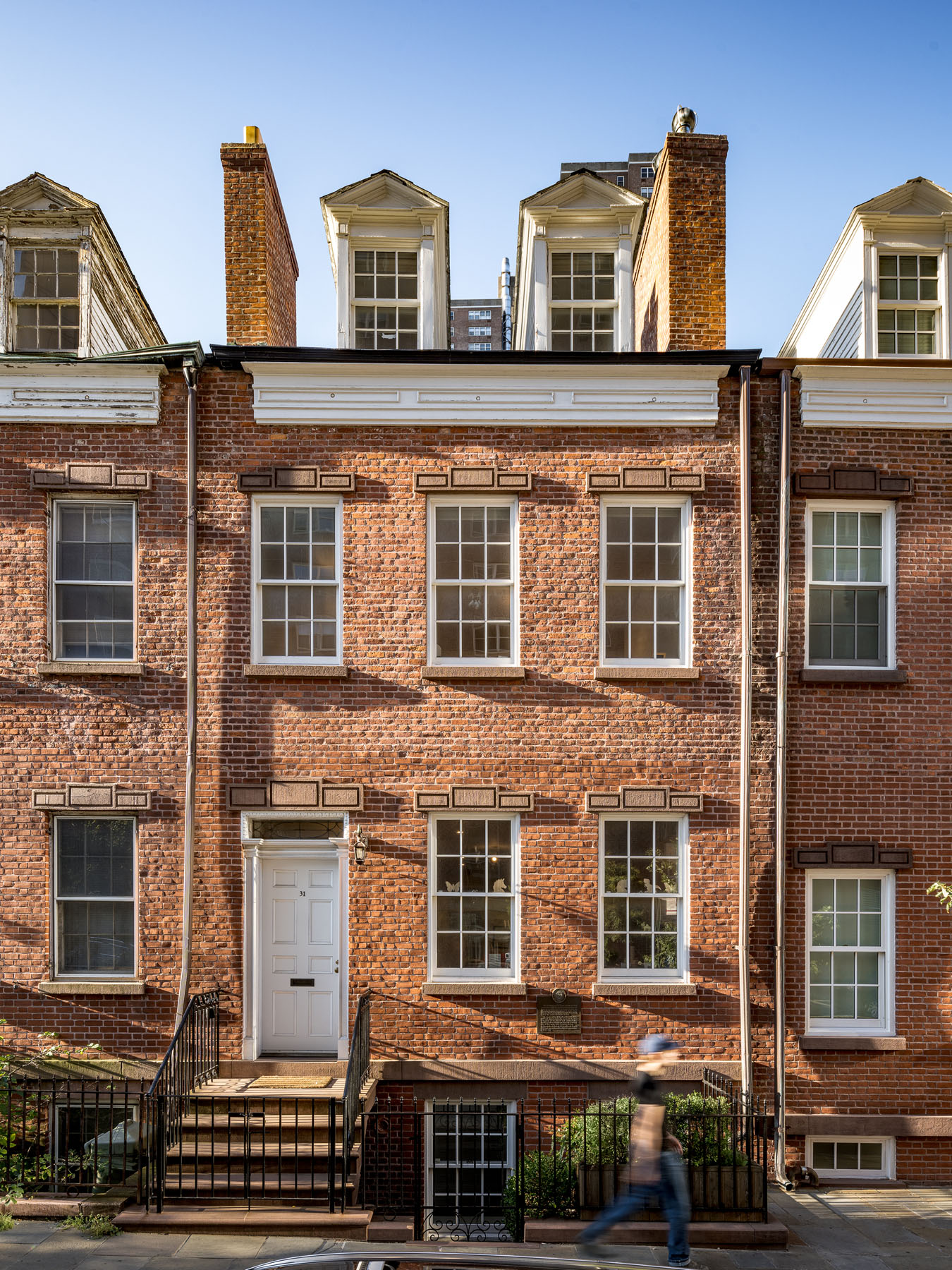 Exterior view of a renovated 1820s Federal Style townhouse in NYC's historic Tribeca townhouse on Harrison Street, showcasing classic brickwork, white trimmed windows, and skylights with pediment detailing.