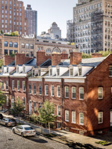 Elevated view of historic brick townhouses on a cobblestone street of Harrison St in Tribeca, juxtaposed against modern high-rises and NYC cityscape in the background.