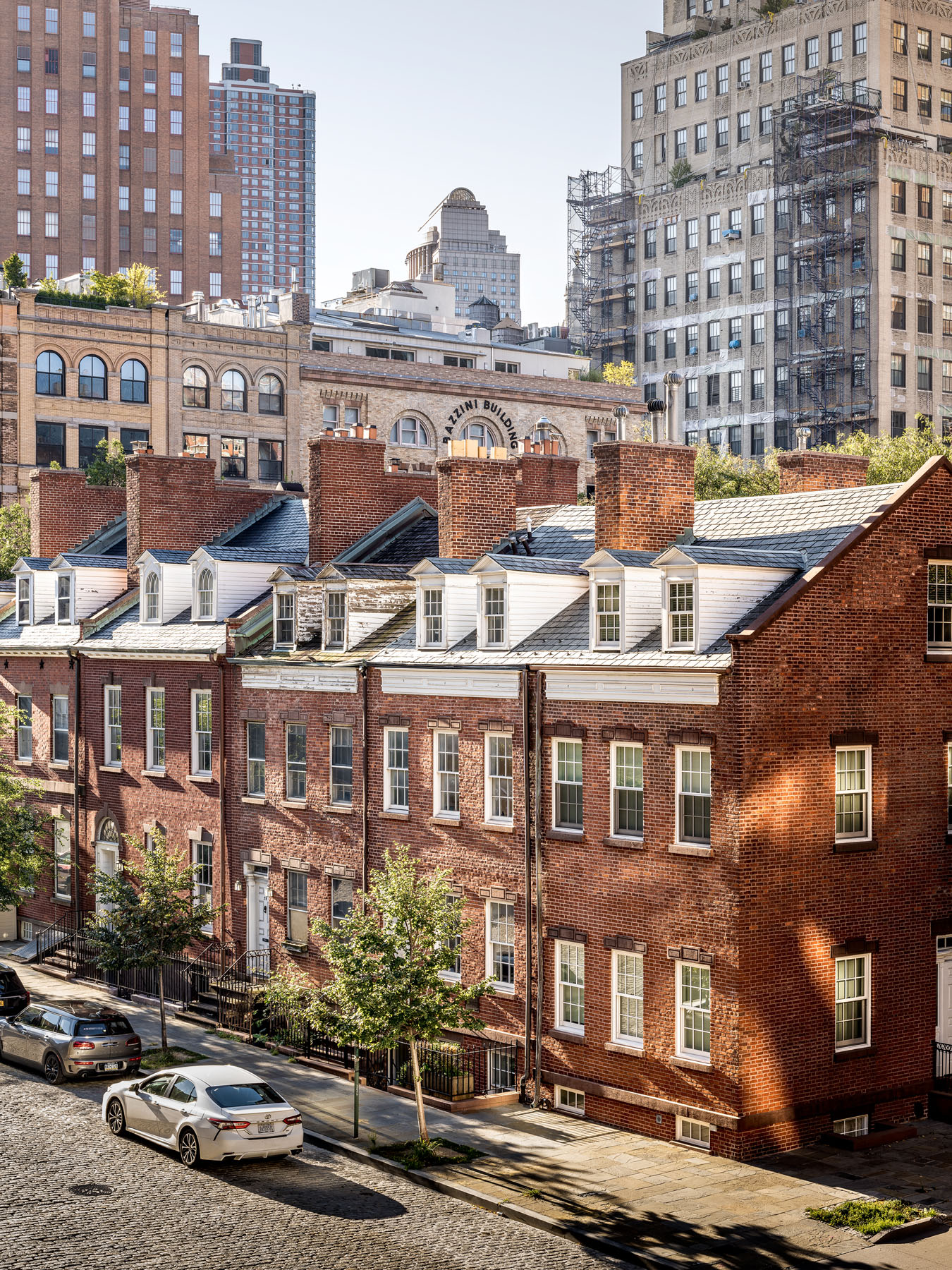 Elevated view of historic brick townhouses on a cobblestone street of Harrison St in Tribeca, juxtaposed against modern high-rises and NYC cityscape in the background.