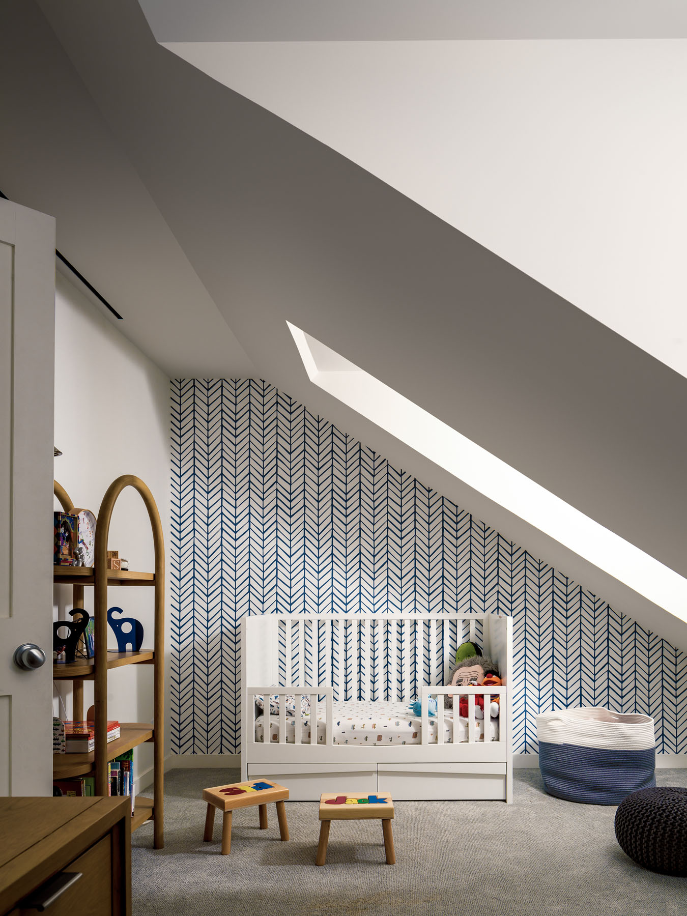 Contemporary children's bedroom in NYC's historic Tribeca townhouse on Harrison Street with sloping ceiling design, geometric patterned accent wall, wooden furniture, and white crib under skylight.