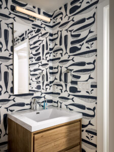 Modern bathroom in NYC's historic Tribeca townhouse on Harrison Street with distinctive whale-patterned wallpaper, sleek wooden vanity, white rectangular sink, and cylindrical overhead light fixture.