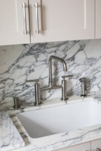 Detailed view of a kitchen sink with marble backsplash and countertop, stainless steel faucet, and white cabinetry in an Upper East Side renovation by Rauch Architecture.