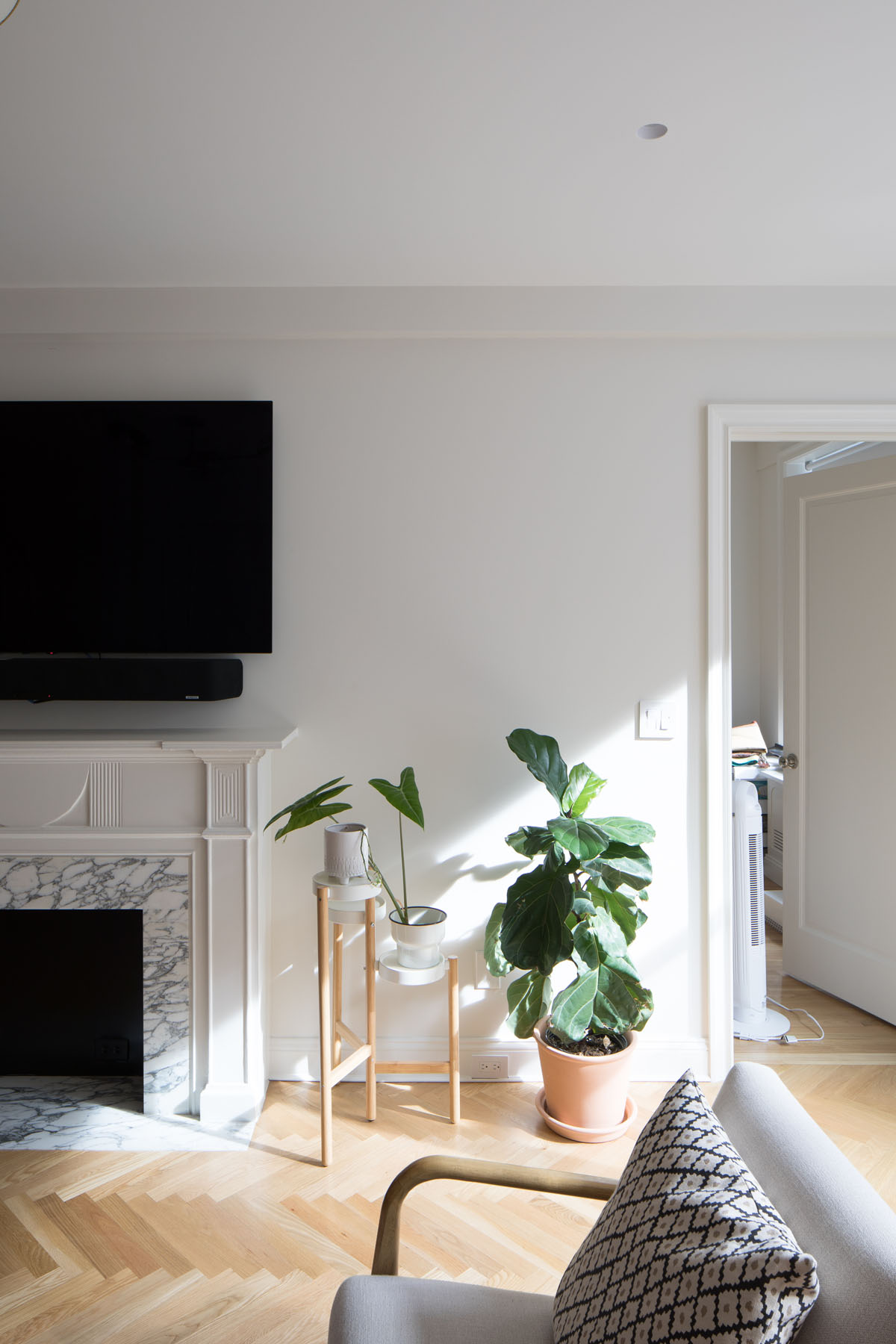 Spacious living room in Upper East Side co-op featuring a large window, traditional fireplace, mid-century modern chairs, and a decorative rug, designed by Rauch Architecture.