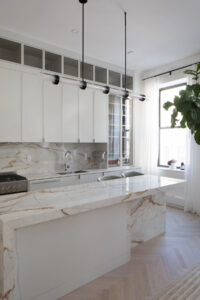 Chelsea duplex kitchen with white shaker cabinets, marble island, and contemporary lighting over herringbone floors by Rauch Architecture.