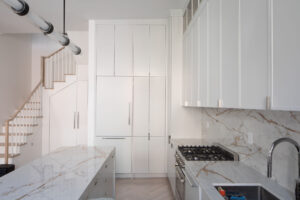 Modern kitchen with white shaker cabinets, marble backsplash, and a view of the staircase in a Chelsea, NYC duplex by Rauch Architecture.