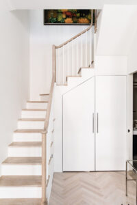 Architecturally integrated staircase with wooden steps and a white storage cabinet in a Chelsea, NYC duplex by Rauch Architecture.