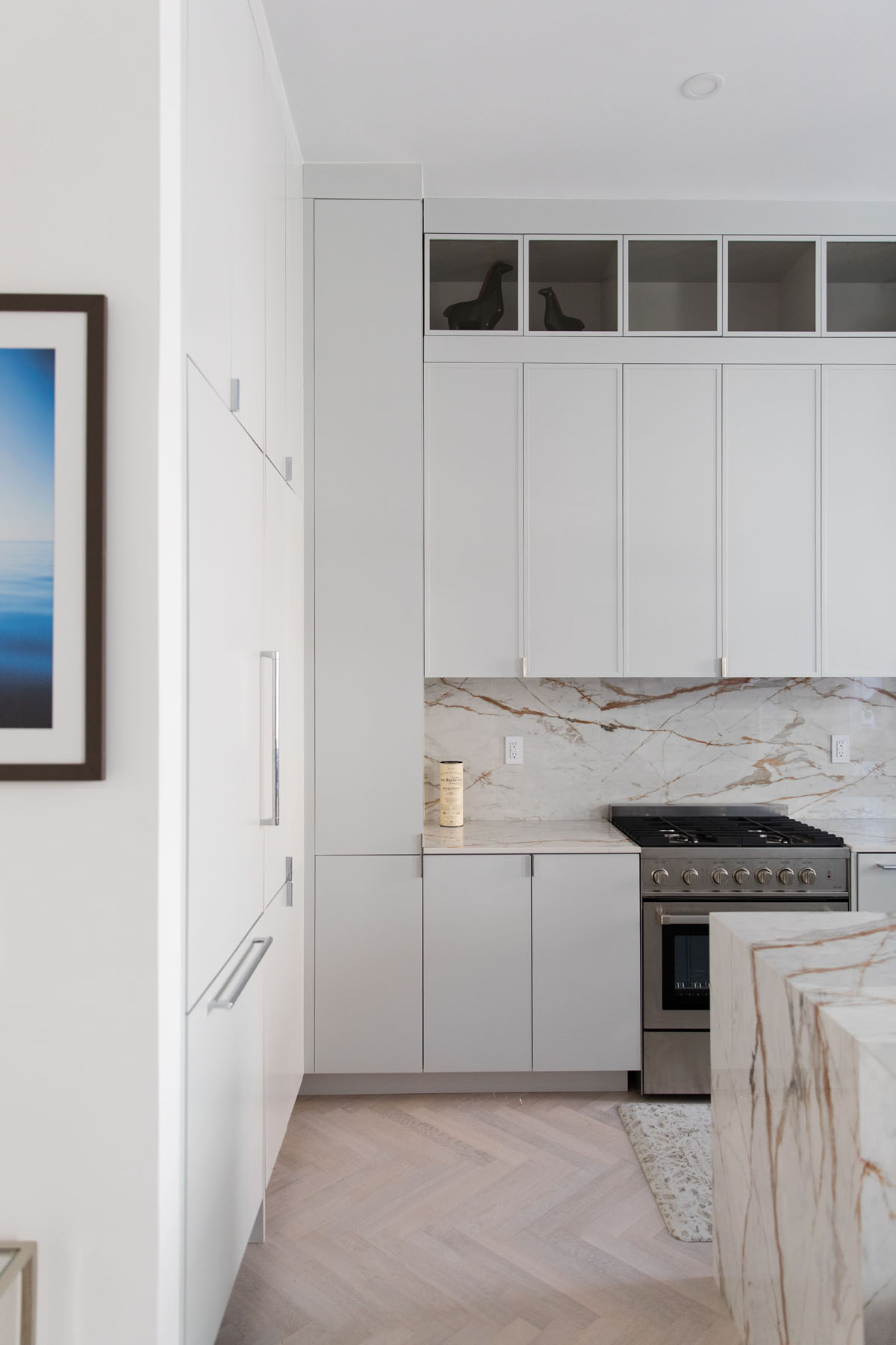 White kitchen with slim shaker cabinets, marble countertops, and backsplash, plus a glass cabinet display in a Chelsea, NYC duplex by Rauch Architecture.