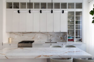 White kitchen with slim shaker cabinets, marble countertops, and backsplash, plus a glass cabinet display in a Chelsea, NYC duplex by Rauch Architecture.