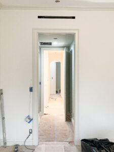 Ongoing interior renovation of a duplex in Chelsea, NYC, focusing on a long, narrow hallway with minimalist aesthetics and trimless doors. The photo captures construction details including exposed ductwork and protective floor coverings, typical of a high-end residential remodel.