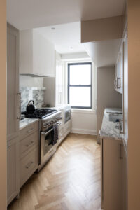 Contemporary Upper East Side kitchen with marble backsplash, stainless steel appliances, white cabinetry, and chevron wood flooring by Rauch Architecture.