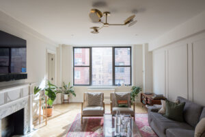 Spacious living room in Upper East Side co-op featuring a large window, traditional fireplace, mid-century modern chairs, and a decorative rug, designed by Rauch Architecture.